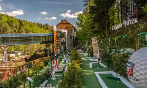 Mini golf z atrakcjami, budynek i las w tle.