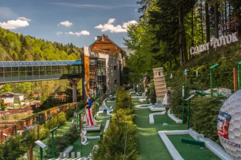 Mini golf z atrakcjami, budynek i las w tle.