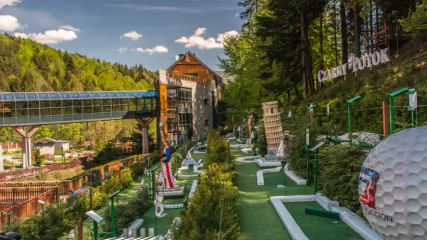 Mini golf z atrakcjami, budynek i las w tle.